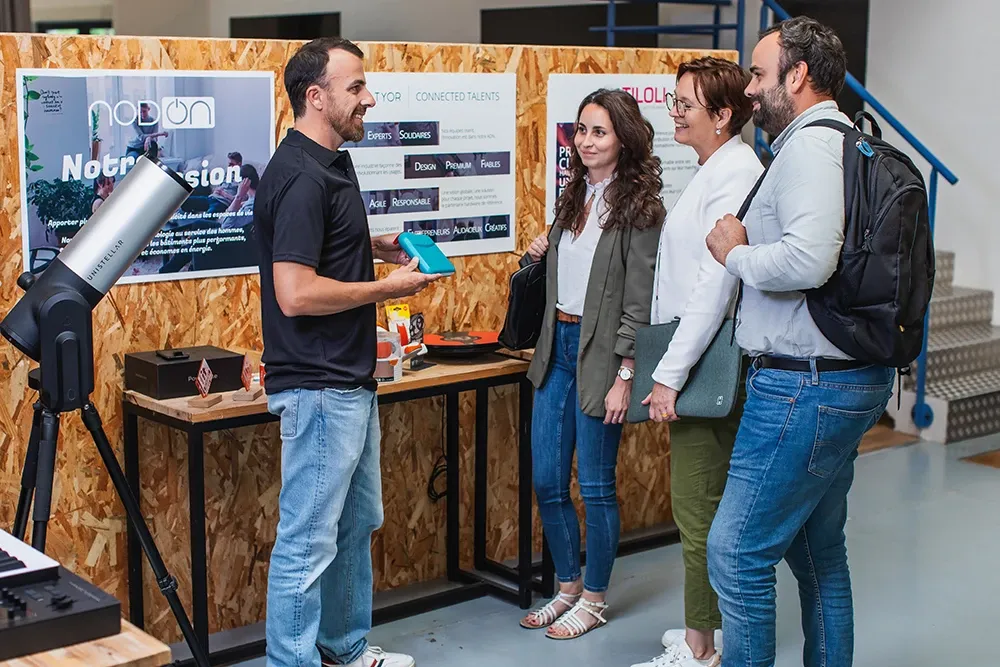 Un collaborateur Altyor présente un produit à trois visiteurs devant des panneaux NodOn et Tiloli