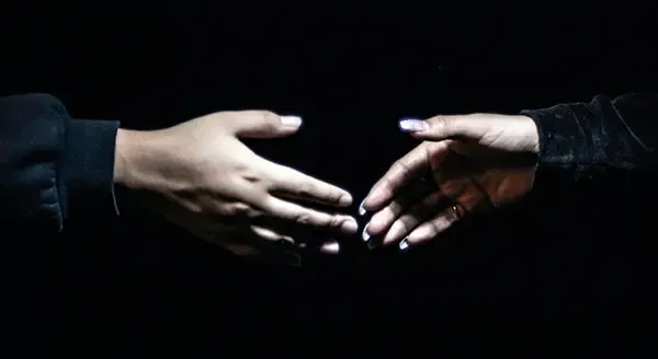Two hands reaching towards each other against a black background