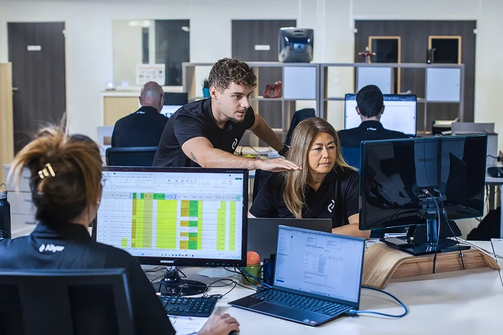 Altyor team in an open-plan office: an employee leans towards a colleague’s screen to discuss a tracking chart