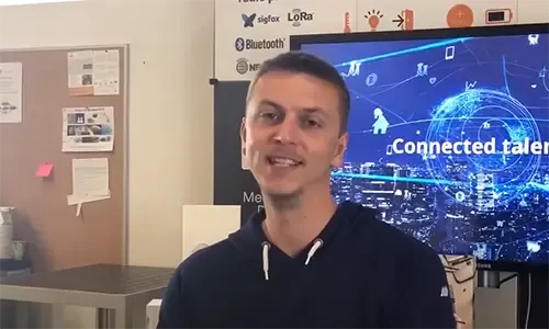 An employee smiling at the camera in front of a screen showing “Connected talent”