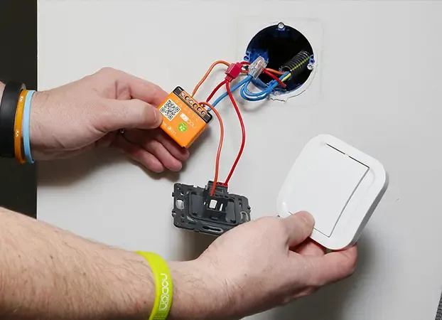 Hands wiring an orange NodOn micromodule to a wall switch