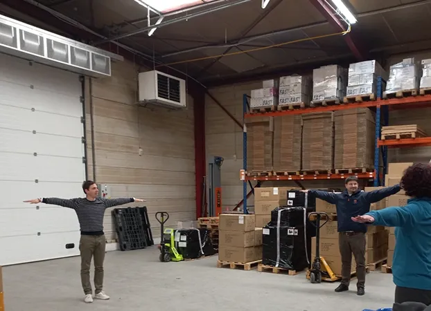 Employees doing a stretching exercise, arms outstretched, in the warehouse