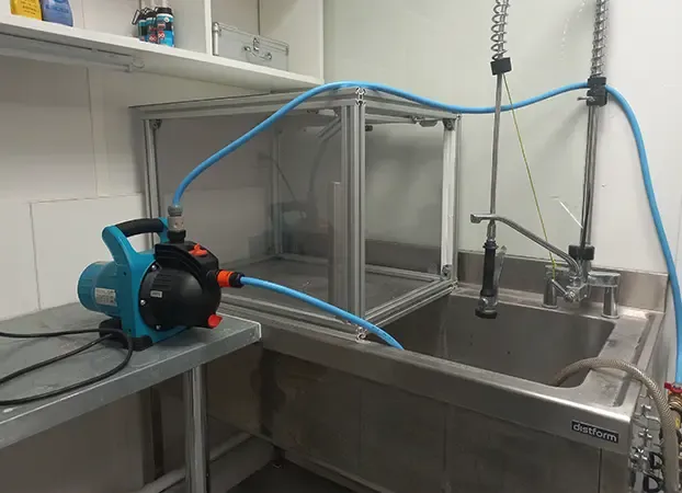 Leak-test bench in the qualification laboratory: glass enclosure over a stainless steel sink, connected to a pump by blue hoses