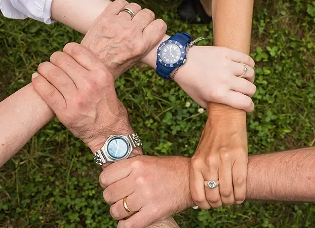 Employees’ hands holding each other by the wrists in a circle, above the grass