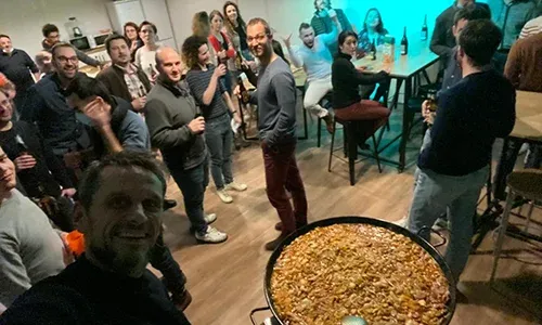 Employees gathered at an evening event around a large paella pan